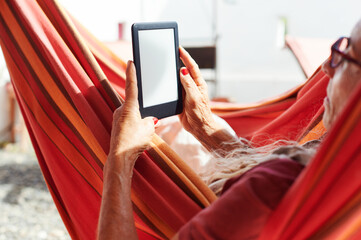 Senior woman reading an e-book in a hammock