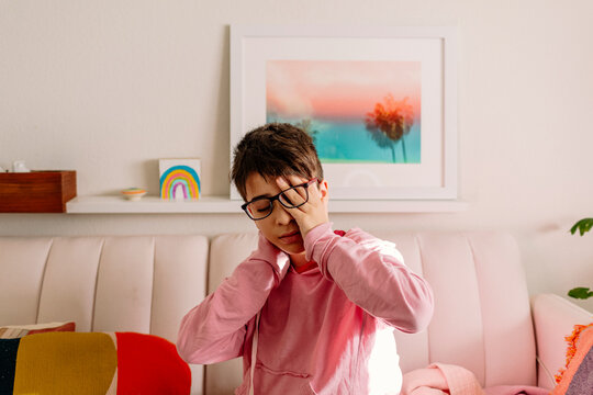 Tired boy with eyeglasses covering one eye while in pink sofa
