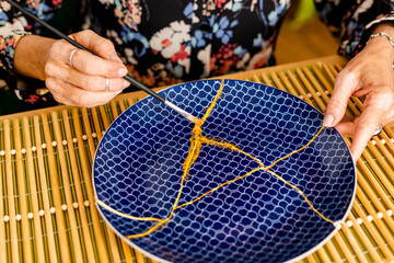 Top view of senior woman hands repairing a broken plate with gold