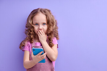 Wow, amazing app for kids. Surprised little kid girl using smartphone with shocked expression, playing game on mobile device, pleasantly surprised by easy application, closing mouth.