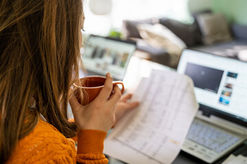 Young woman working from home in living room checking invoice in front of laptop