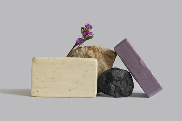 Handmade white and purple soap bar laying, balancing on rock, gray background, copy space. Solid shampoo, oil on podium. Organic, natural cosmetic. Beauty, skincare product