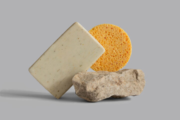 Handmade soap bar, yellow sponge laying, balancing on rock, gray background, copy space. Solid shampoo, oil on podium. Organic, natural cosmetic. Beauty, skincare product