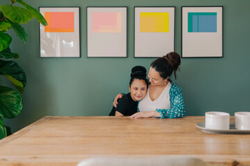 Portrait Mother and pre-teen daughter hugging and sitting by a colorful  gallery wall