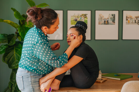 Mother applying makeup to daughter pre-teen in dining table