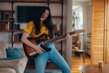 Woman playing a guitar and dancing in her living room while having fun at home