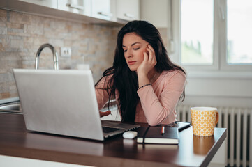 Woman sitting in the kitchen in the morning in her pajamas and using a laptop