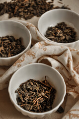 Pile of dried green tea leaves in little bowls, white background, dried tea leaves