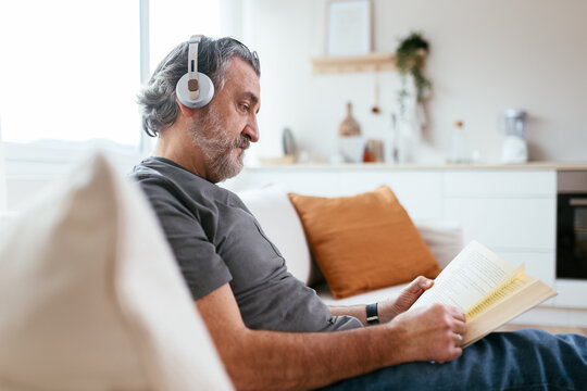 Serious bearded man reading book on sofa