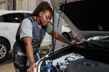 Fototapeta na wymiar Tired african auto mechanic woman misunderstanding what is wrong with car, looking inside of hood, side view portrait. Young female in auto service. copy space