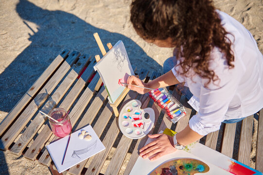 High angle view of a female painter using watercolor technique to paint a picture in open air on the beach