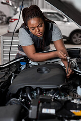 Fototapeta na wymiar Afro American Professional Mechanic Woman Working on Vehicle in Car Service. Female Engine Specialist Fixing Motor, Wearing Overalls and Using a Ratchet. Modern Clean Workshop.