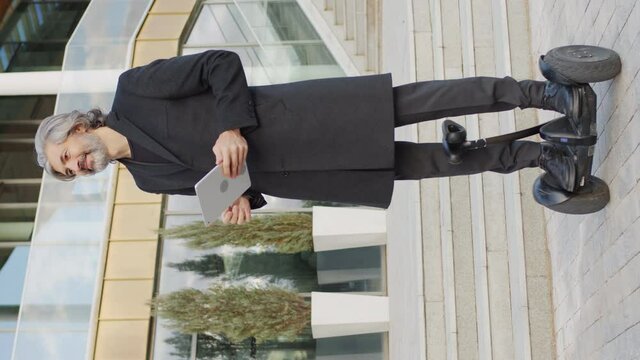 Vertical slowmo full shot of mature caucasian man standing outside on gyroscooter controlling it with digital tablet