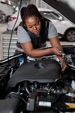 Afro American Professional Mechanic Woman Working on Vehicle in Car Service. Female Engine Specialist Fixing Motor, Wearing Overalls and Using a Ratchet. Modern Clean Workshop.