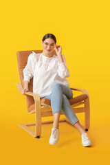 Fototapeta na wymiar Young woman sitting in armchair on color background
