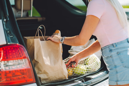 Unrecognizable woman put her shopping eco bags with food into car trunk on a parking.
