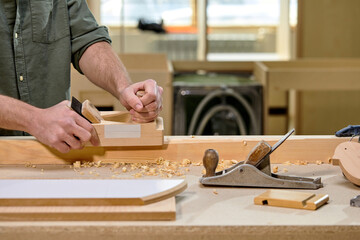 Carpenter working in workshop, young caucasian man planing and shaving a piece of wood. Joinery work on production of wooden furniture. Small Business Concept. copy space. close-up hands