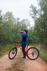 Fototapeta na wymiar Young man drinking water on his bike on a forest road, active lifestyle.