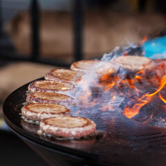 Burgers for hamburger prepared on bbq grill, barbecue outdoors with fire flame