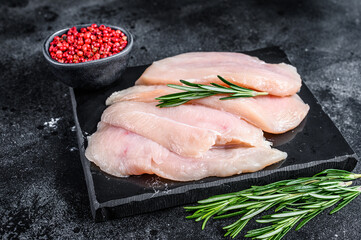 Raw sliced chicken breast fillet steaks on a marble board. Black background. Top view