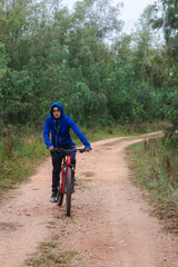 Young man with headphones riding a bike on a forest road, playing sports in nature.