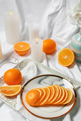 Sliced juicy oranges and burning candles on fabric background