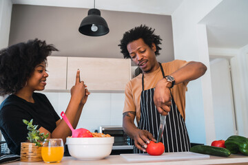 Afro woman taking photo of her husband while he prepares dinner.