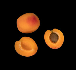 Ripe Apricot fruits, one whole apricot and two divided apricot pieces, on a black background in isolation