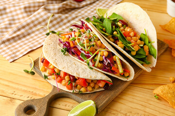 Board with tasty vegetarian tacos on light wooden background