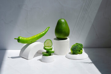 Balanced nutrition concept. Play of shadows and sunlight. Green fresh fruit and vegetables on light gray background. Cucumber, hot pepper, avocado, herb, and broccoli.