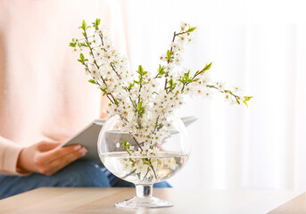 Vase with beautiful blooming branches on table in room