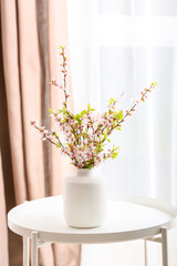 Vase with beautiful blooming branches on table in room