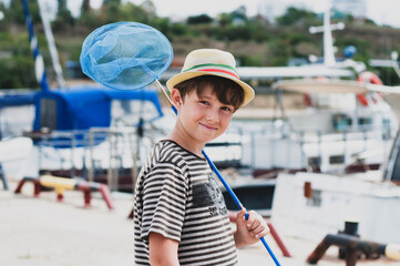 Happy boy in a hat with Italian flag, a striped T-shirt stands on the yacht pier with a fishing...