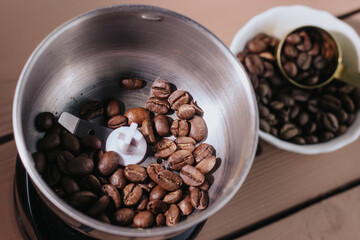 Coffee beans in a white plate on a wooden background and an electric coffee grinder. Iron spoon for coffee beans. Coffee content, coffee shop.