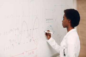 African American woman math teacher univercity writing on blackboard with marker.