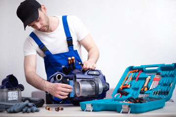 Handsome young serviceman is repairing modern vacuum cleaner in his office