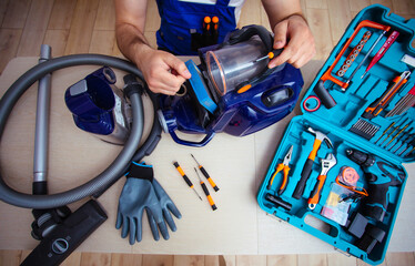 Handsome young serviceman is repairing modern vacuum cleaner in his office