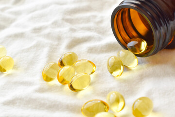 Evening primrose oil capsules spilling out of an amber glass bottle on fabric background.  Copy space is on the left. 