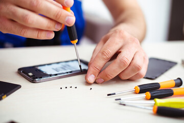 Close up photo of specialist man while he is repairing broken smartphone on his workplace with professional tools