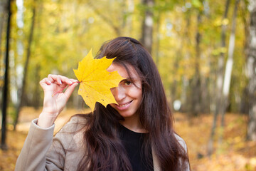 Brunette woman in autumn park with yellow leaf. Close plan. Smiling woman. Autumn mood. Beautiful brunette.