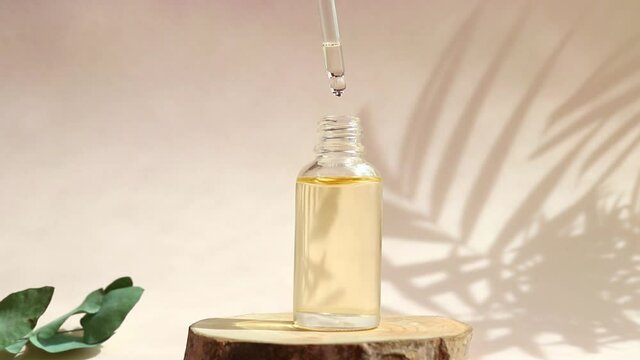Bottle of cosmetic essential oil with dropper on a wood cut close-up. Serum oil is dripping from dropper. Hard light. Beauty concept. Serum skin care product