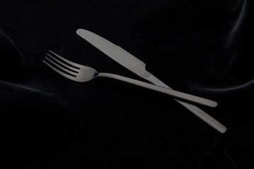 Black fork and knife on the black tablecloth.