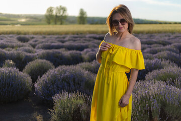 Beautiful and pretty young woman in yellow dress relaxes and enjoys walk in the lavender field at...