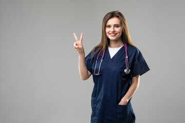 Young doctor woman smiling and showing victory sign on isolated on grey background