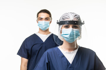Two doctors of both sexes in white lab coat and protective mask looks on each other standing with arms folded on white background.