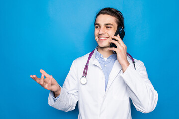 Medical doctor wearing white coat and stethoscope talking on phone standing isolated over blue background