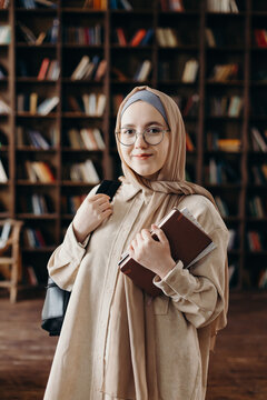 Content young Muslim female student standing with book in library