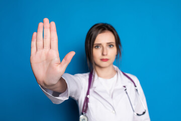 attractive woman doctor showing stop gesture refusing standing in blue background