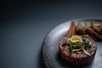 closeup of beef steak tartare with raw egg yolk on plate on black background