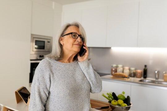 senior woman using cellphone in the kitchen - Powered by Adobe